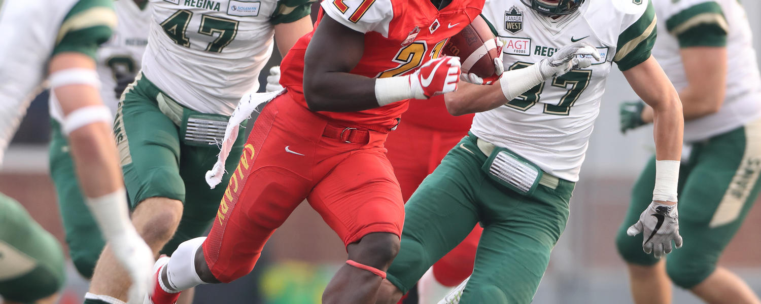 Dinos football player running with the football being chased by opponents