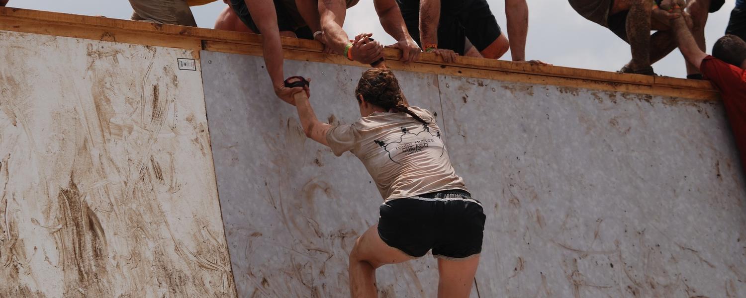 woman being pulled up on an obstacle during an obstacle course race