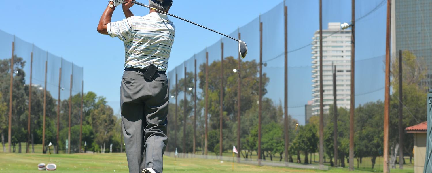 Older gentleman swing a golf club at a driving range