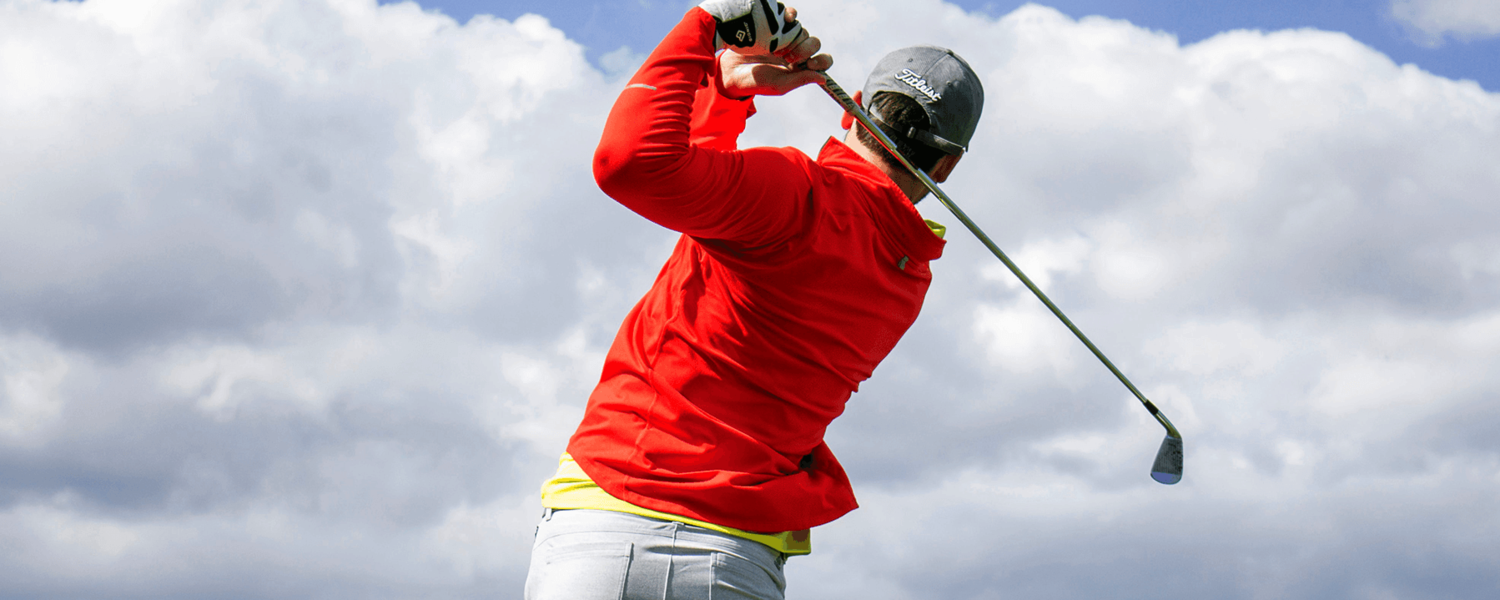 man in red shirt swinging golf club